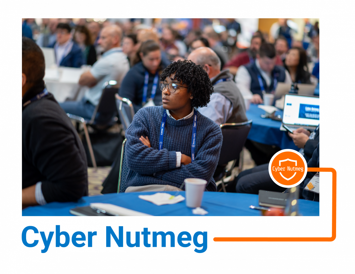 Photo of a person sitting at a table with their arms crossed listening to a speaker on stage, with the caption, 'Cyber Nutmeg'